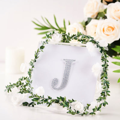 Decorative letter "J" with rhinestones surrounded by floral accents.