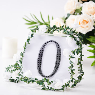 Decorative number zero surrounded by greenery and white flowers.