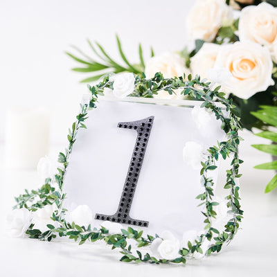 Table number card adorned with greenery and flowers, featuring the number one.