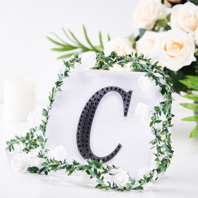 Decorative letter "C" surrounded by greenery and flowers on a white background.