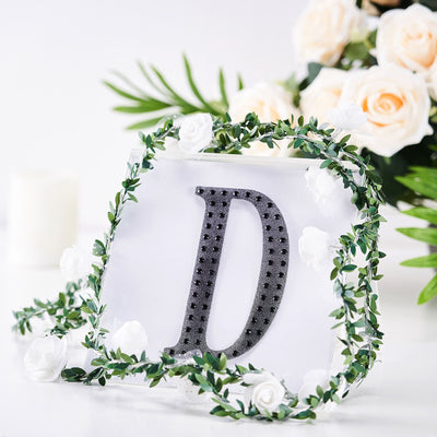 Decorative letter "D" adorned with flowers and greenery on a white background.