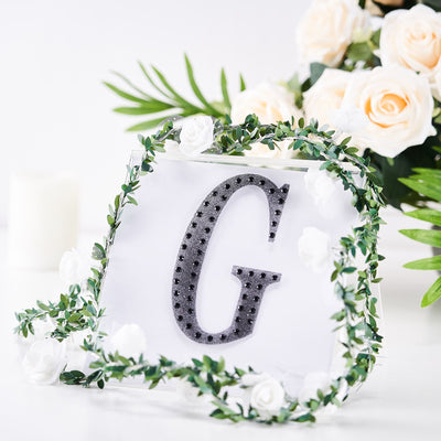 Decorative letter "G" with floral accents on a clear display.