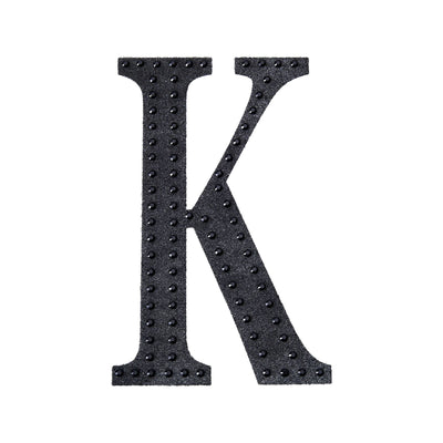 Black decorative letter "K" with studded design on a white background