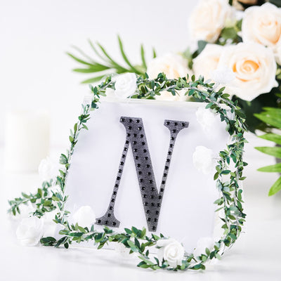 Decorative letter "N" surrounded by greenery and flowers.