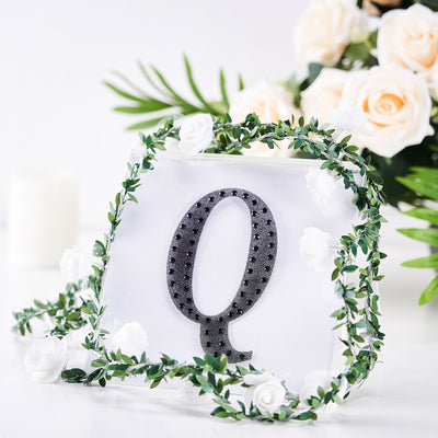 Decorative letter Q with floral accents and greenery on a white background.
