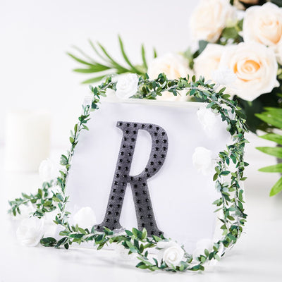 Decorative letter "R" surrounded by greenery and flowers.