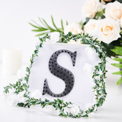 Black letter "S" decorative sign surrounded by greenery and flowers.