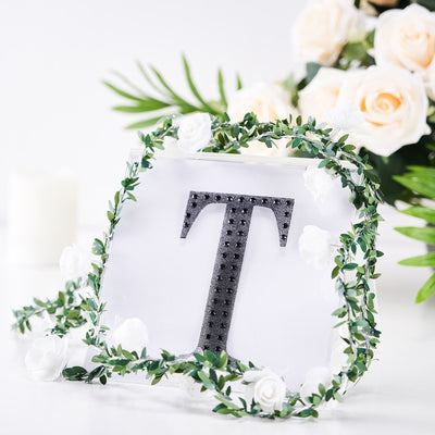 Personalized acrylic letter "T" adorned with greenery and white flowers.