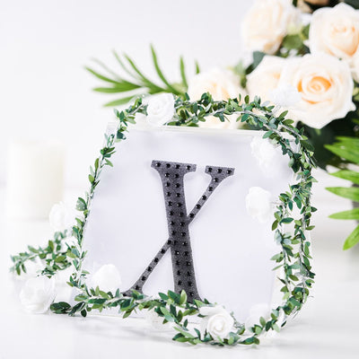 Decorative letter "K" surrounded by greenery and white roses.