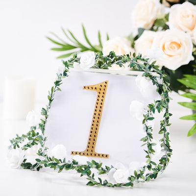Gold table number "1" surrounded by greenery and white flowers.