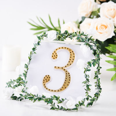 Gold table number three surrounded by greenery and flowers.