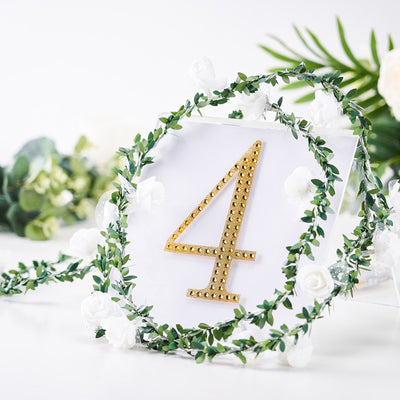 Gold rhinestone table number 4 surrounded by greenery and white flowers