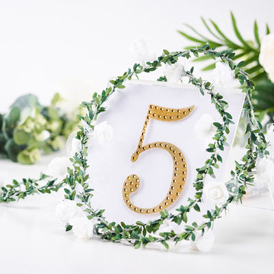 Gold number 5 decor surrounded by greenery and white flowers.
