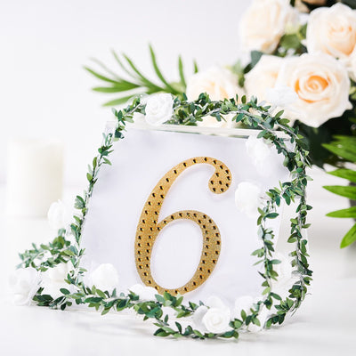 Gold table number 6 surrounded by greenery and white roses.