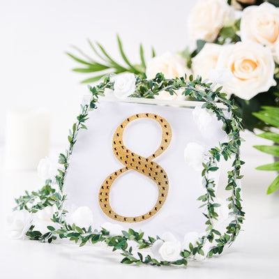 Gold table number 8 with floral accents and greenery on a white background.