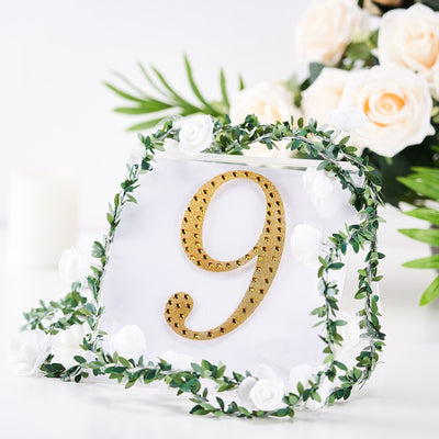 Gold table number 9 adorned with greenery and white flowers.