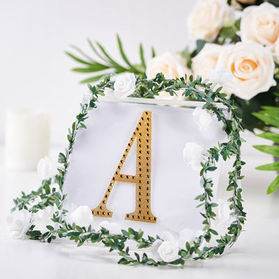 Gold letter "A" decorated with faux flowers and greenery, ideal for events or decor.