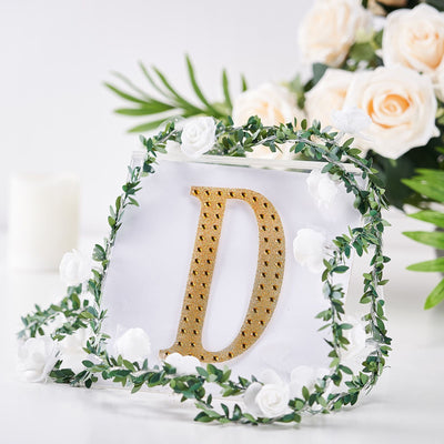 Gold letter "D" decor surrounded by greenery and white roses.
