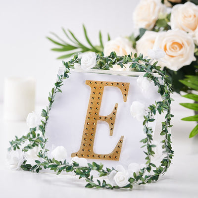 Gold letter "E" decor with floral accents on a white background.