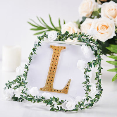Gold letter "L" decoration surrounded by greenery and flowers.