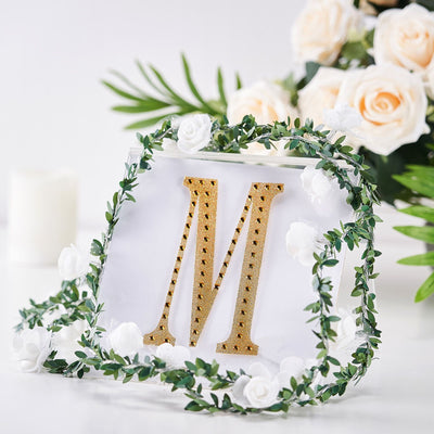 Gold letter "M" decoration surrounded by flowers and greenery.