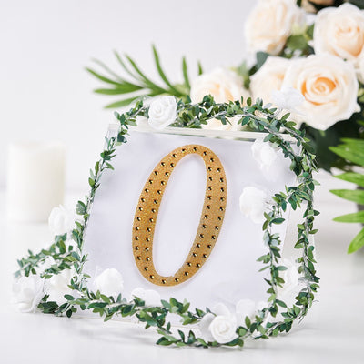 Gold studded number "0" surrounded by decorative greenery and flowers.
