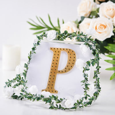 Gold letter "P" surrounded by greenery and white roses in a decorative setting.