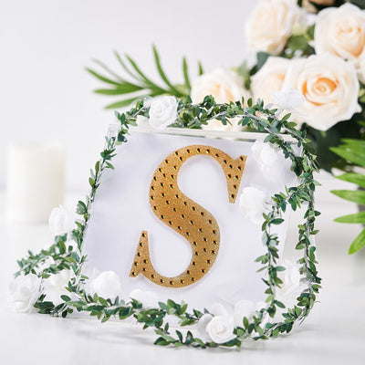 Gold letter "S" in a decorative frame with floral accents.