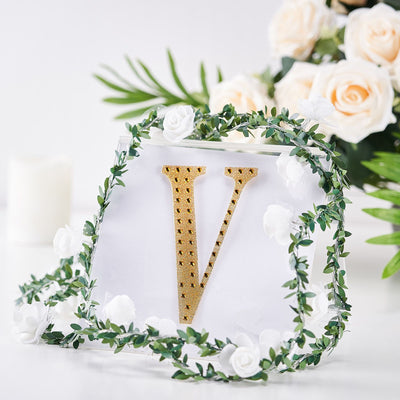 Gold letter "V" surrounded by floral decor on a white background.