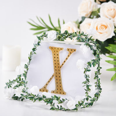 Gold letter X with floral decoration on a clear background.