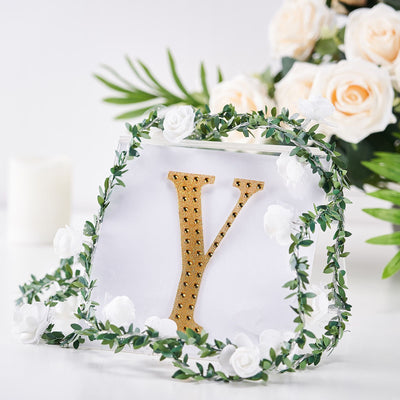 Gold letter "Y" adorned with greenery and white flowers on a clear backdrop.