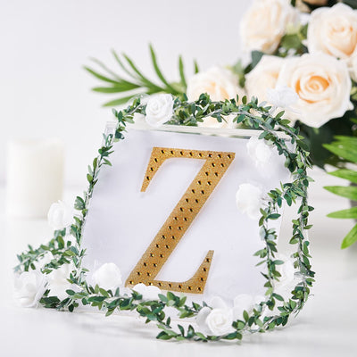 Gold letter "Z" adorned with greenery and white roses on a transparent backdrop.