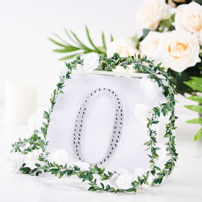 Decorative number "0" surrounded by greenery and flowers on a white background.