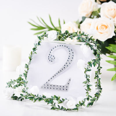 Table number two with rhinestones surrounded by greenery and white flowers.