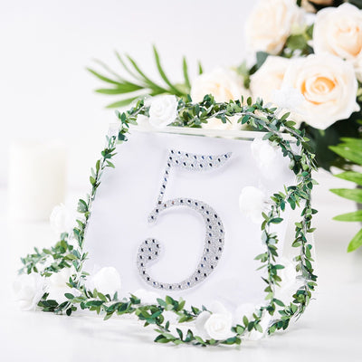 Elegant table number 5 adorned with greenery and white flowers.