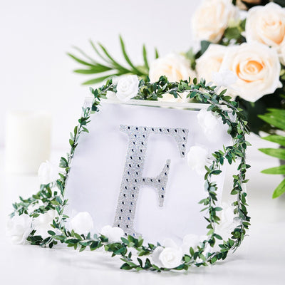 Decorative letter "F" with rhinestones surrounded by floral garland.