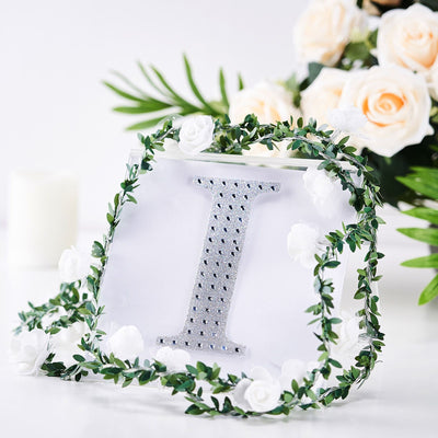Decorative letter "I" with rhinestones and floral accents against a white background.
