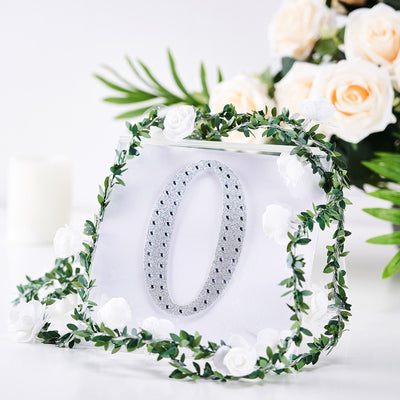Decorative number '0' with rhinestones, surrounded by floral greenery.