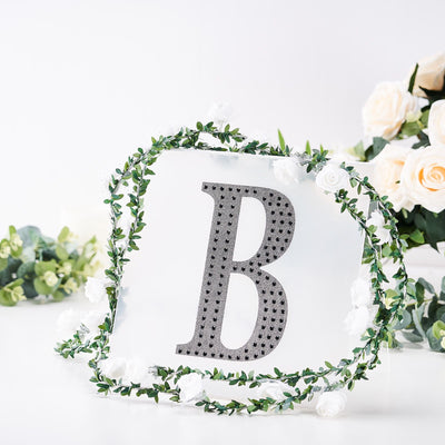 Decorative letter "B" adorned with flowers and greenery on a white background.