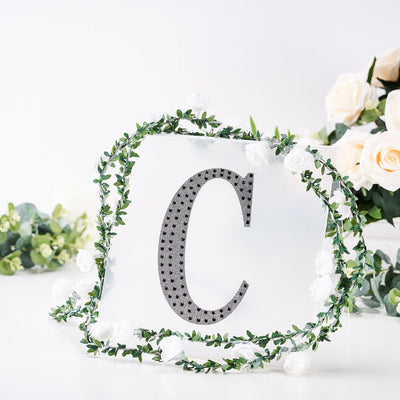 Decorative letter "C" surrounded by greenery and white flowers