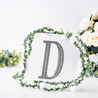 Decorative letter "D" surrounded by floral garland on a plain background.