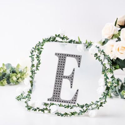 Decorative letter 'E' surrounded by artificial flowers and greenery.