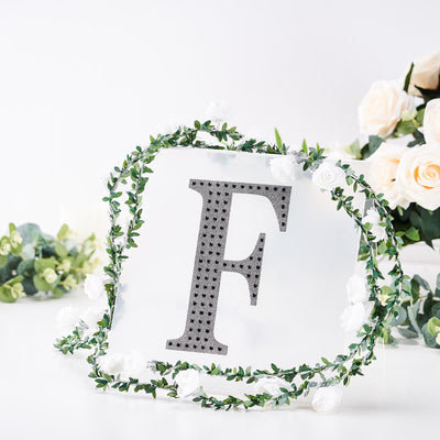 Decorative letter "F" surrounded by greenery and flowers.