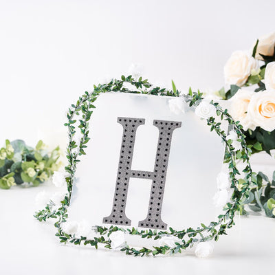 Decorative letter "H" surrounded by flowers and greenery