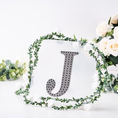 Decorative letter "J" surrounded by flowers and greenery on a white background.