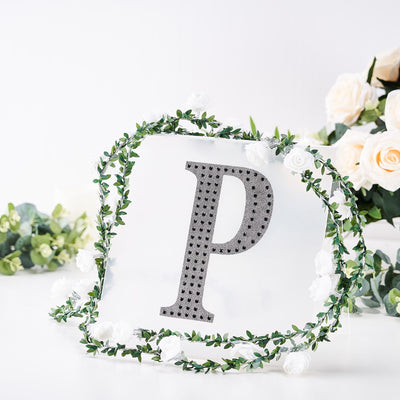 Decorative letter "P" surrounded by greenery and flowers.