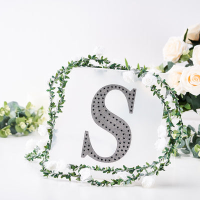 Decorative letter "S" surrounded by greenery and flowers.