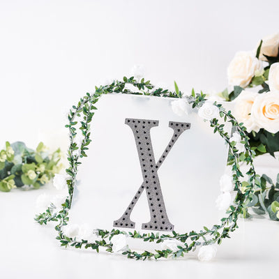 Decorative letter X with floral accents on a white background.