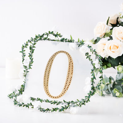 Clear acrylic number "0" with gold trim, surrounded by floral greenery.