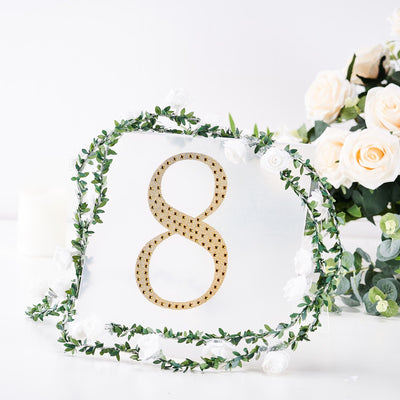 Gold number 8 decoration surrounded by floral garland on a white background.